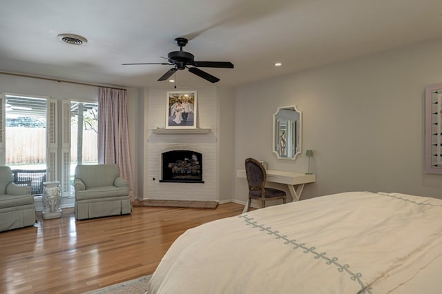 bedroom with a large fireplace, ceiling fan, and light hardwood / wood-style flooring