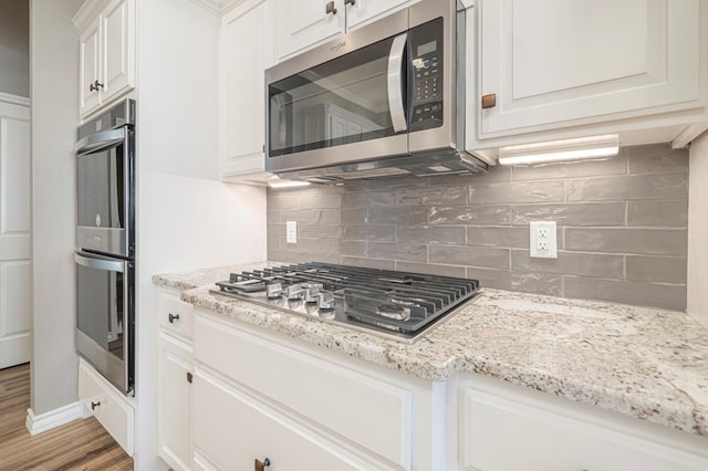 kitchen featuring white cabinetry, stainless steel appliances, light stone counters, tasteful backsplash, and light wood-type flooring