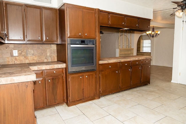 kitchen with oven, tasteful backsplash, a ceiling fan, a chandelier, and light tile patterned flooring