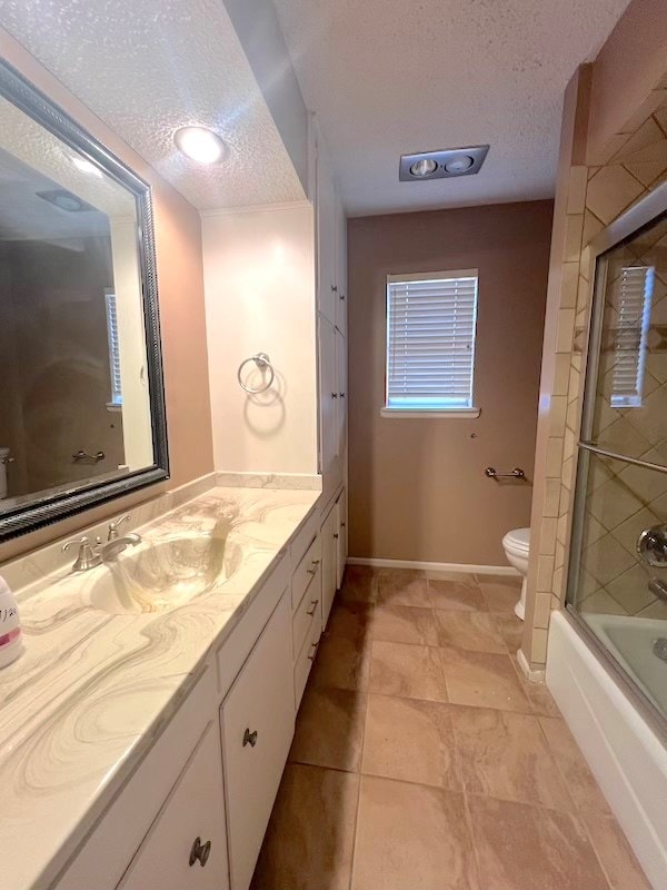 full bathroom featuring a textured ceiling, toilet, vanity, and combined bath / shower with glass door