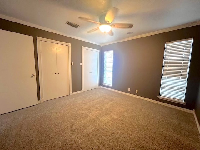 unfurnished bedroom with ceiling fan, ornamental molding, carpet flooring, and two closets