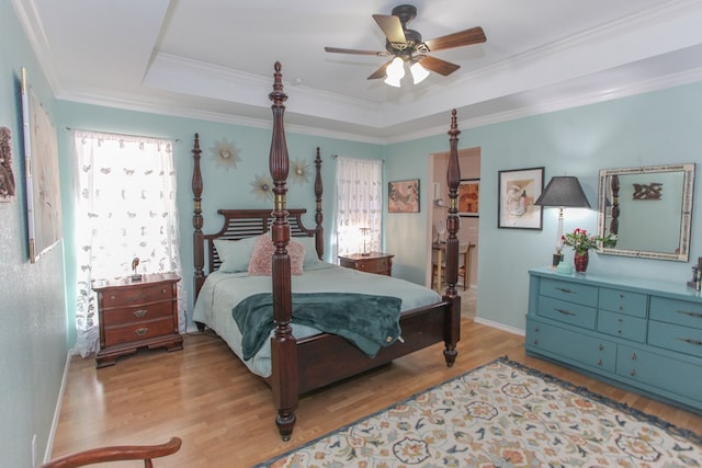 bedroom featuring light wood-style floors, a tray ceiling, ornamental molding, and baseboards