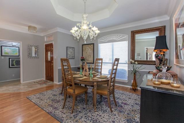 dining area featuring light wood-style floors, a raised ceiling, a notable chandelier, and ornamental molding