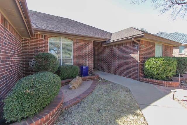 property entrance with a shingled roof and brick siding