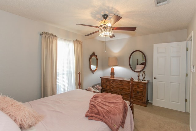 bedroom featuring light colored carpet, visible vents, ceiling fan, and a textured ceiling