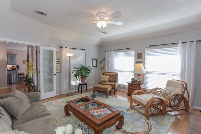 living room featuring a ceiling fan, visible vents, vaulted ceiling, and light wood finished floors