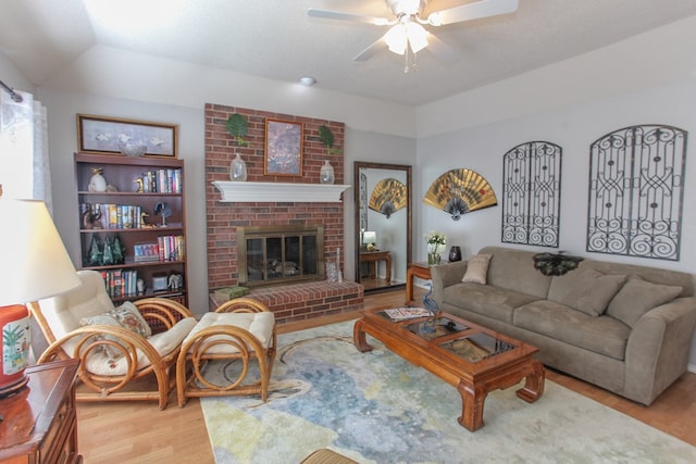 living area featuring light wood-style flooring, a fireplace, ceiling fan, and a textured ceiling