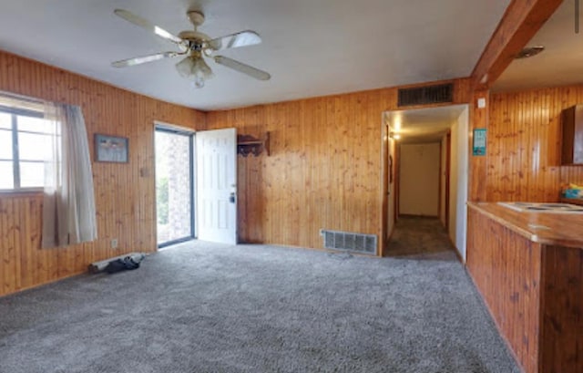 1518 Stadium Ave, Big Spring, TX 79720 - unfurnished living room with carpet floors, wood walls, a ceiling fan, and beam ceiling