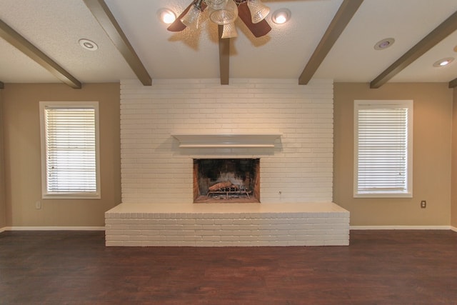 unfurnished living room featuring a textured ceiling, a brick fireplace, beam ceiling, dark wood-type flooring, and ceiling fan