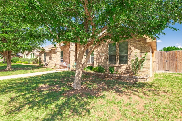 view of property hidden behind natural elements featuring brick siding, a front lawn, and fence