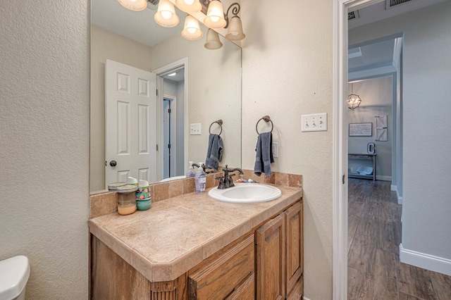 half bathroom with a textured wall, vanity, a chandelier, baseboards, and wood finished floors