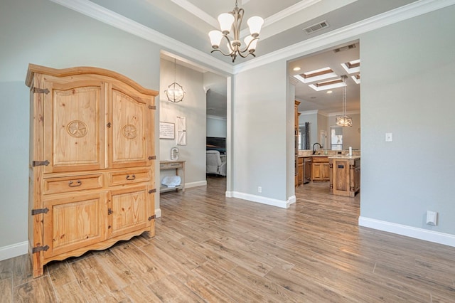 spare room with a notable chandelier, ornamental molding, light wood-style flooring, and visible vents