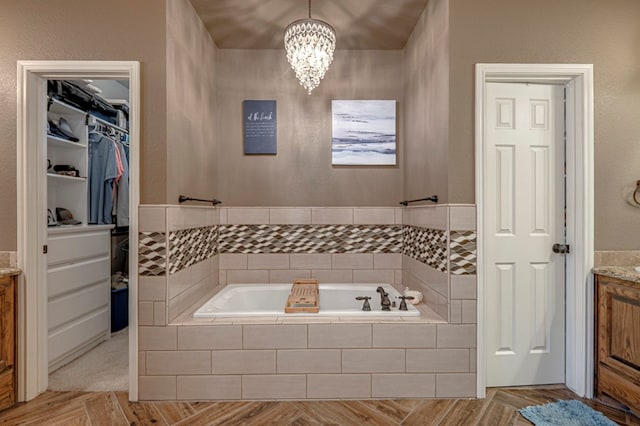 full bath with vanity, a garden tub, a notable chandelier, and a spacious closet