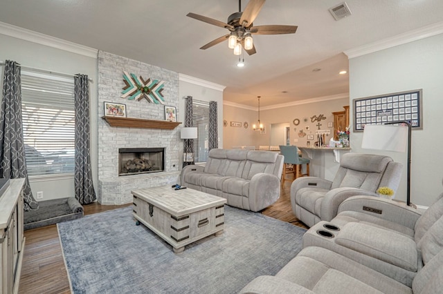 living room featuring ceiling fan, visible vents, a fireplace, wood finished floors, and ornamental molding