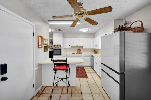 kitchen with a peninsula, light countertops, white cabinets, a ceiling fan, and stainless steel appliances