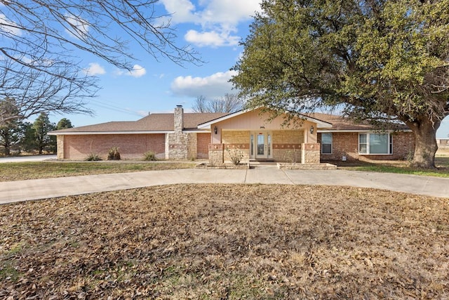 ranch-style house with driveway, stone siding, a chimney, and brick siding