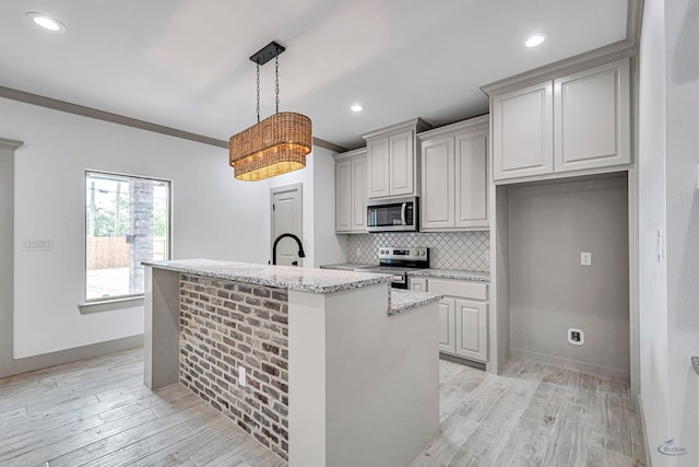 603 S Benton, Midland, TX 79701 - kitchen with appliances with stainless steel finishes, tasteful backsplash, light wood-style flooring, a center island with sink, and light stone countertops