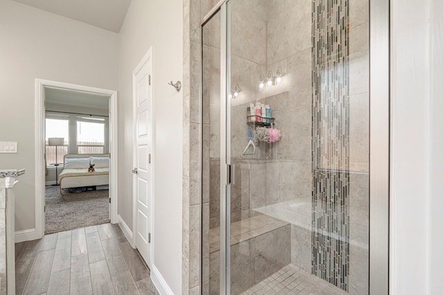 ensuite bathroom with connected bathroom, baseboards, wood finished floors, and a stall shower