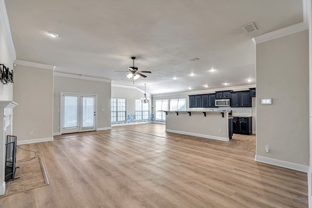 unfurnished living room featuring ceiling fan with notable chandelier, lofted ceiling, light hardwood / wood-style flooring, and crown molding