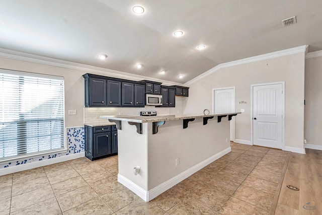 kitchen featuring a kitchen island with sink, light stone countertops, vaulted ceiling, ornamental molding, and a breakfast bar