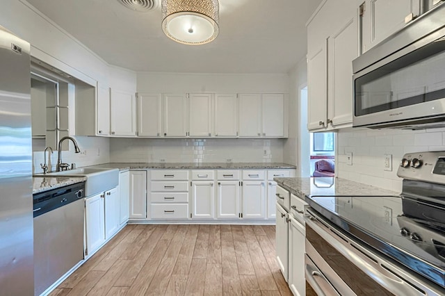 710 W Nobles Ave, Midland, TX 79701 - kitchen with stainless steel appliances, a sink, light wood-style floors, white cabinets, and decorative backsplash