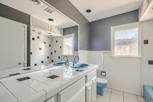 710 W Nobles Ave, Midland, TX 79701 - bathroom featuring toilet, double vanity, tile patterned floors, and a wainscoted wall