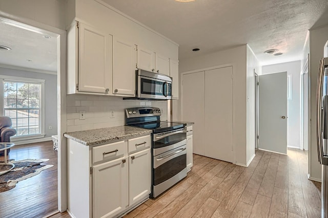 710 W Nobles Ave, Midland, TX 79701 - kitchen with appliances with stainless steel finishes, light wood-style flooring, white cabinets, ornamental molding, and decorative backsplash