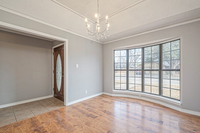 empty room featuring crown molding, a textured ceiling, wood finished floors, a chandelier, and baseboards