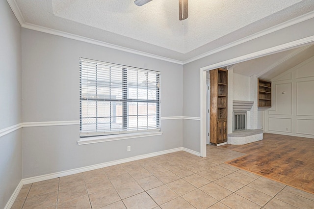 unfurnished living room featuring a fireplace with raised hearth, ceiling fan, light tile patterned floors, a textured ceiling, and baseboards