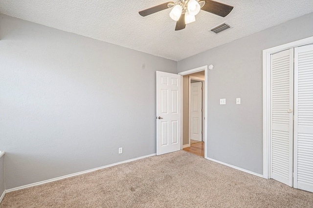 unfurnished bedroom featuring a textured ceiling, light colored carpet, visible vents, baseboards, and a closet