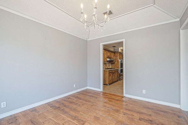 spare room with ornamental molding, a textured ceiling, wood finished floors, a chandelier, and baseboards