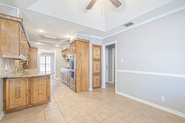 kitchen with light stone counters, a tray ceiling, visible vents, and brown cabinets