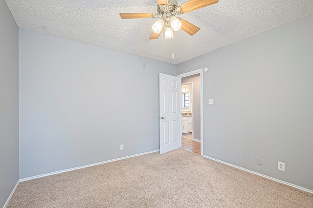 empty room featuring light carpet, baseboards, a ceiling fan, and a textured ceiling