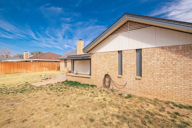 exterior space with brick siding, a chimney, fence, and a lawn