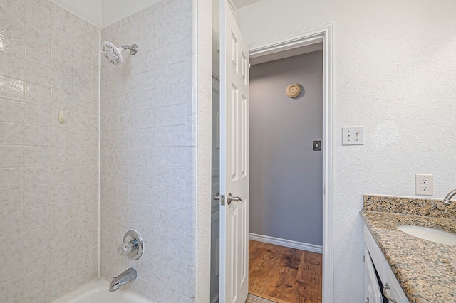 full bath with bathing tub / shower combination, a textured wall, vanity, wood finished floors, and baseboards