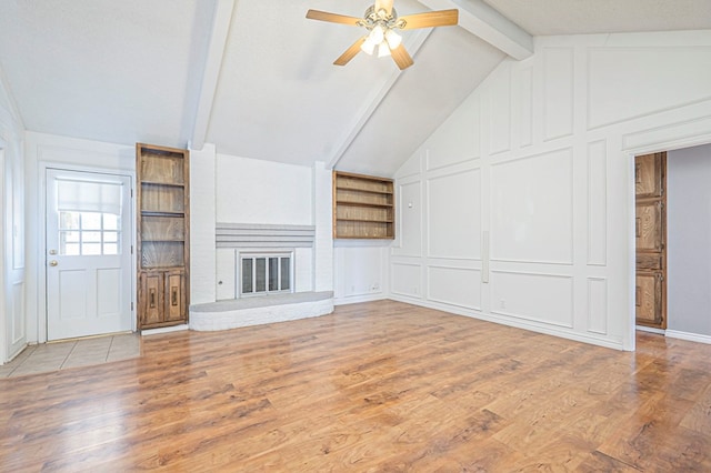 unfurnished living room with lofted ceiling with beams, built in shelves, wood finished floors, and a decorative wall