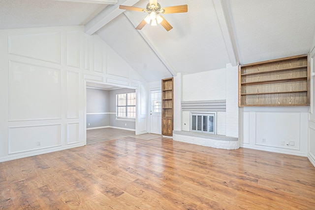 unfurnished living room with built in features, vaulted ceiling with beams, a fireplace, a decorative wall, and wood finished floors