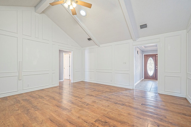 interior space with vaulted ceiling with beams, visible vents, a decorative wall, ceiling fan, and wood finished floors