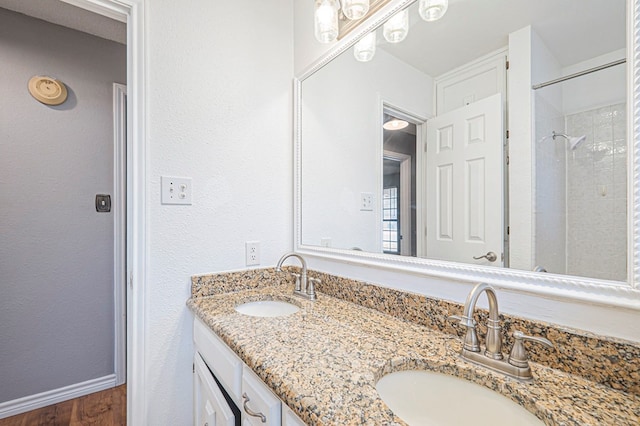 full bath with a textured wall, double vanity, a sink, and baseboards