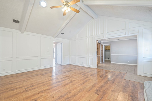 unfurnished living room featuring ceiling fan, a decorative wall, wood finished floors, visible vents, and beam ceiling