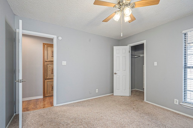 unfurnished bedroom with light carpet, baseboards, a walk in closet, a textured ceiling, and a closet