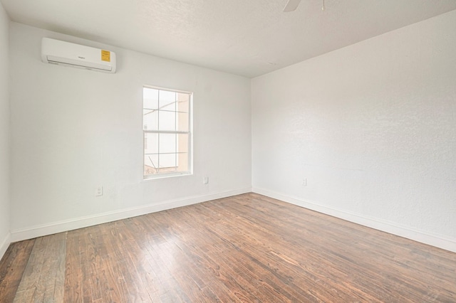 empty room with a wall unit AC, a ceiling fan, a textured ceiling, wood finished floors, and baseboards