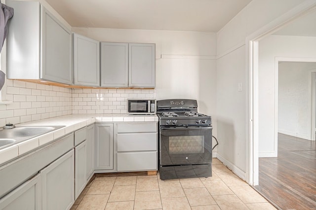 kitchen with tile countertops, light tile patterned floors, black range with gas stovetop, backsplash, and stainless steel microwave