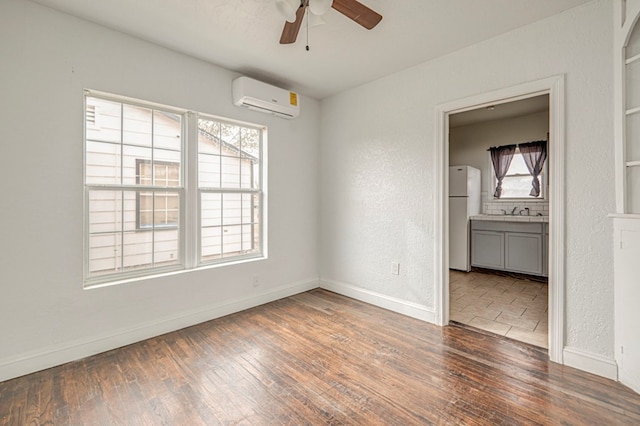 empty room with baseboards, a ceiling fan, a wall unit AC, wood-type flooring, and a sink