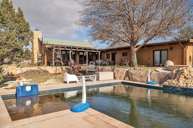 back of property with stucco siding, an outdoor pool, a chimney, and a patio