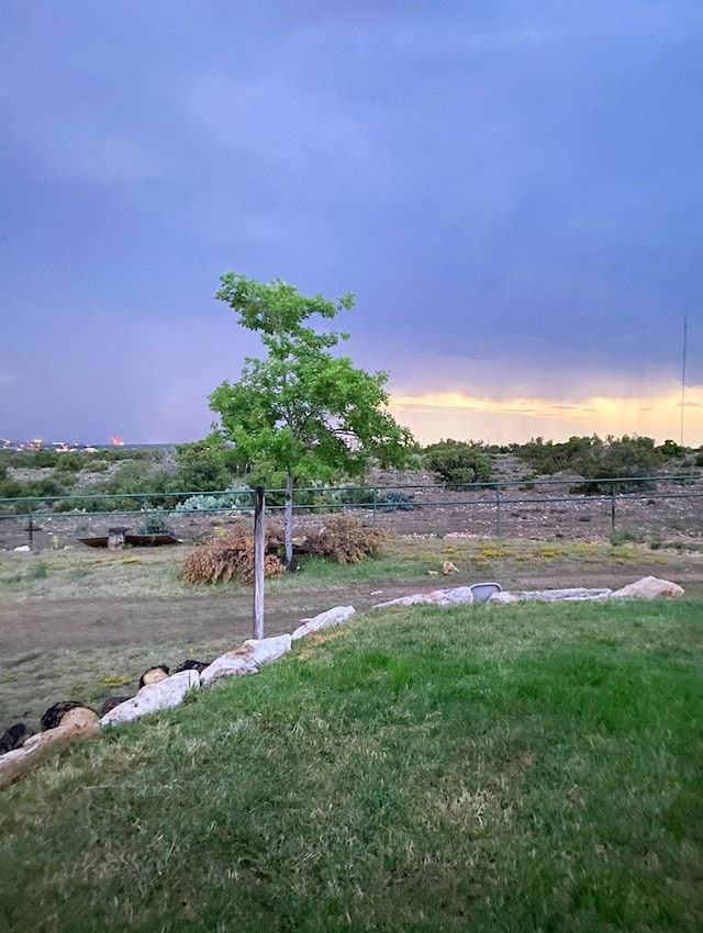 yard at dusk featuring a rural view and fence