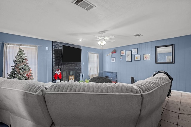 living room with tile patterned floors, ceiling fan, a textured ceiling, and a brick fireplace