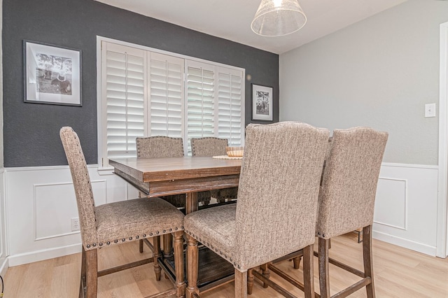 dining space with a wainscoted wall, light wood-style floors, and a decorative wall