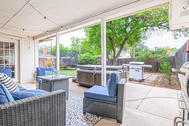 view of patio featuring a trampoline, a fenced backyard, grilling area, a hot tub, and outdoor lounge area