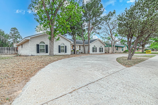 single story home featuring brick siding, curved driveway, and fence